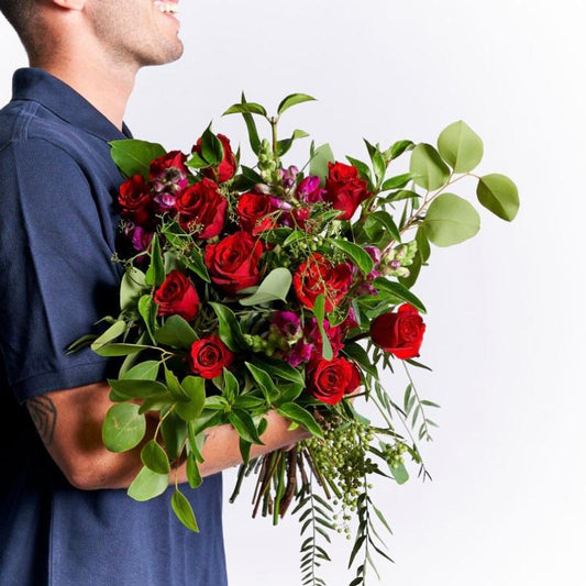 Man holding a large bouquet of red roses and greenery, smiling in profile while wearing a navy shirt.