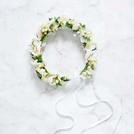 Angelic flower crown made with white and light green artificial flowers, featuring delicate petals and leaves, with a long white ribbon for tying.