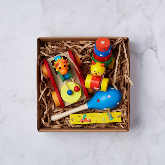 Baby's First Toy Set displayed in a cardboard box with wooden toys including a giraffe roller, stacking rings, maraca, and whistle. Perfect for early learning and play.