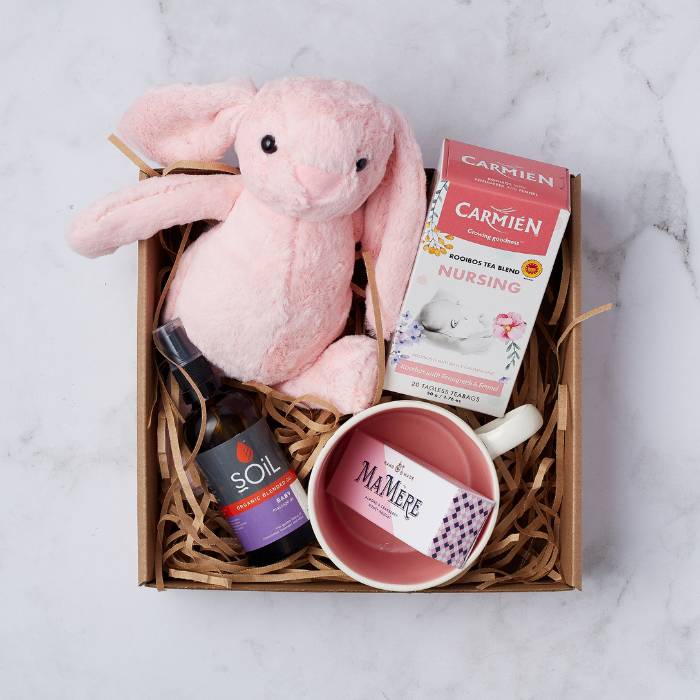 Blissful Mum & Baby Set featuring a soft pink plush bunny, Carmién Nursing Rooibos Tea, SOiL organic baby oil, a pink ceramic cup, and a box of MaMère almond and cranberry nougat, elegantly packed in a kraft gift box.