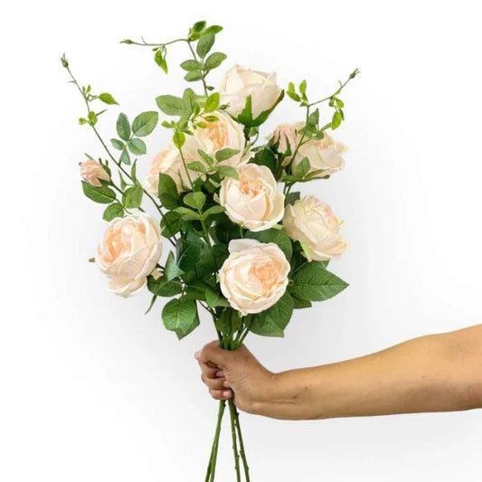 Hand holding a bouquet of lifelike Cabbage Rose Pink Pearl artificial flowers with soft blush petals and vibrant green leaves.