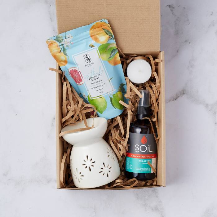 Calm and Peaceful Spa Gift Box featuring grapefruit & lime bath salts, a ceramic oil burner, a tealight candle, and SOiL organic relaxing massage oil, all arranged neatly in a gift box with wood wool packaging.