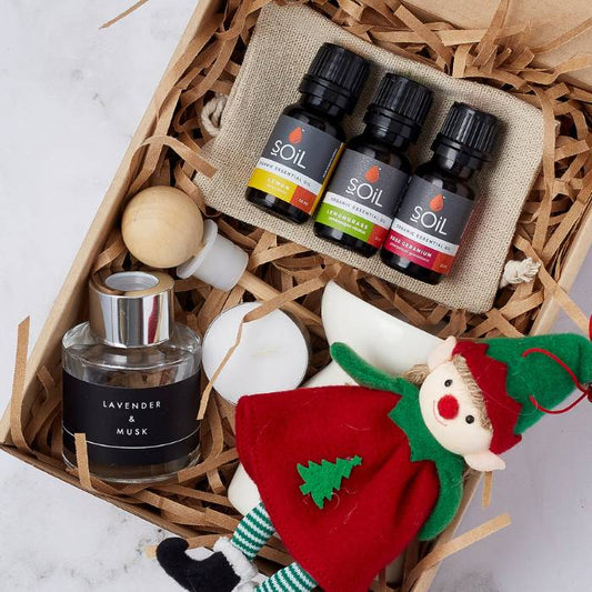 Elegant aromatherapy gift set including SOiL essential oils in lemon, lemongrass, and rose geranium, a lavender and musk diffuser, tea light candles, a wooden dropper, and a festive elf doll.