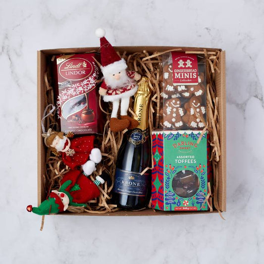 Top-down view of the Christmas Spirit Gift Box for Him with festive treats including Lindt chocolate, Krone sparkling wine, gingerbread cookies, and holiday ornaments.