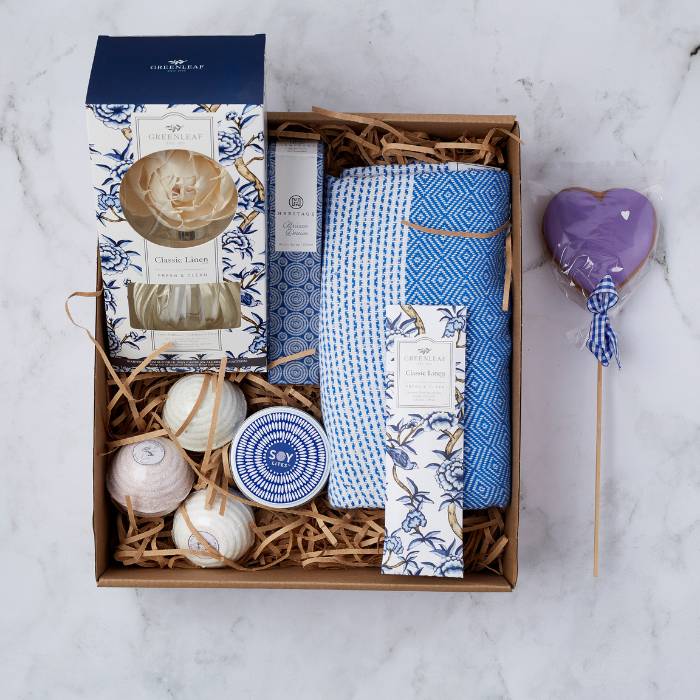 Decadence Delight Gift Set featuring Greenleaf Classic Linen products, blue cotton throw, soy candle, bath bombs, and a heart-shaped cookie.