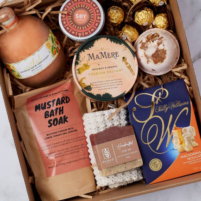 Close-up view of the Deluxe Pamper Gift Box highlighting Turkish delight, macadamia nougat, handmade soap, mustard bath soak, Ferrero Rocher chocolates, bath salts, and a soy candle for a luxurious self-care experience.