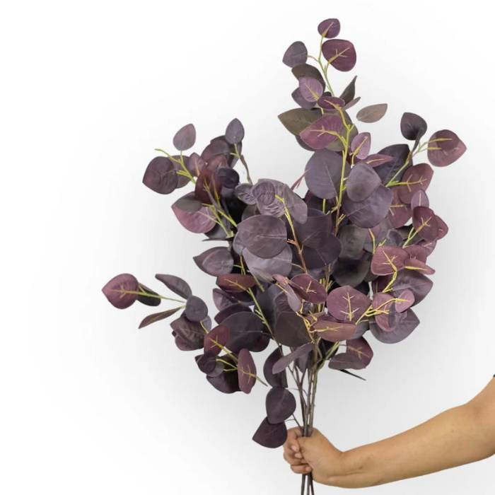 A hand holding a large bouquet of burgundy eucalyptus artificial foliage, highlighting the fullness and rich colour of the leaves.