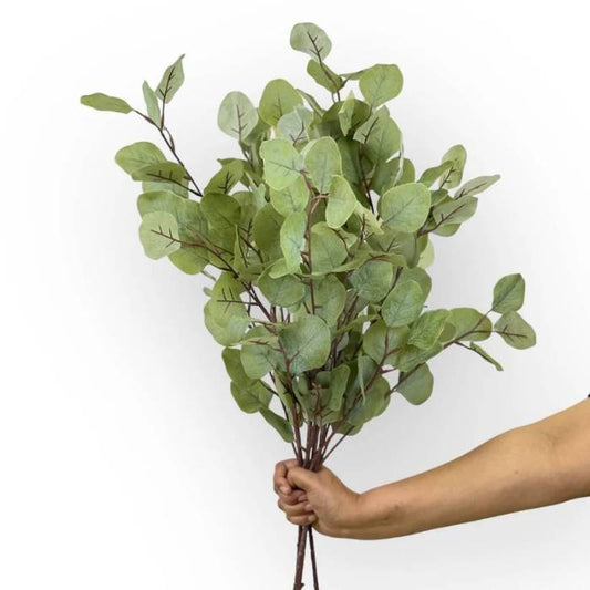 A hand holding a full bouquet of Eucalyptus Grey Green artificial foliage, highlighting the lush and lifelike greenery with soft grey-green tones.