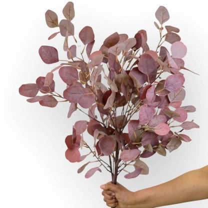 A hand holding a large bouquet of Eucalyptus Light Burgundy artificial foliage, highlighting the rich blend of light burgundy leaves in a full, realistic arrangement.