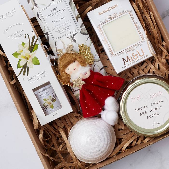 Festive Bliss Spa Gift Box featuring a vanilla reed diffuser, bath bomb, handmade soap, honey scrub, and angel ornament.