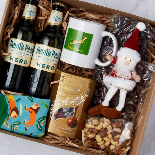 Festive Cheer Hamper with Devil’s Peak non-alcoholic beers, Lindt chocolates, Springbok mug, assorted nuts, socks, and Santa ornament.