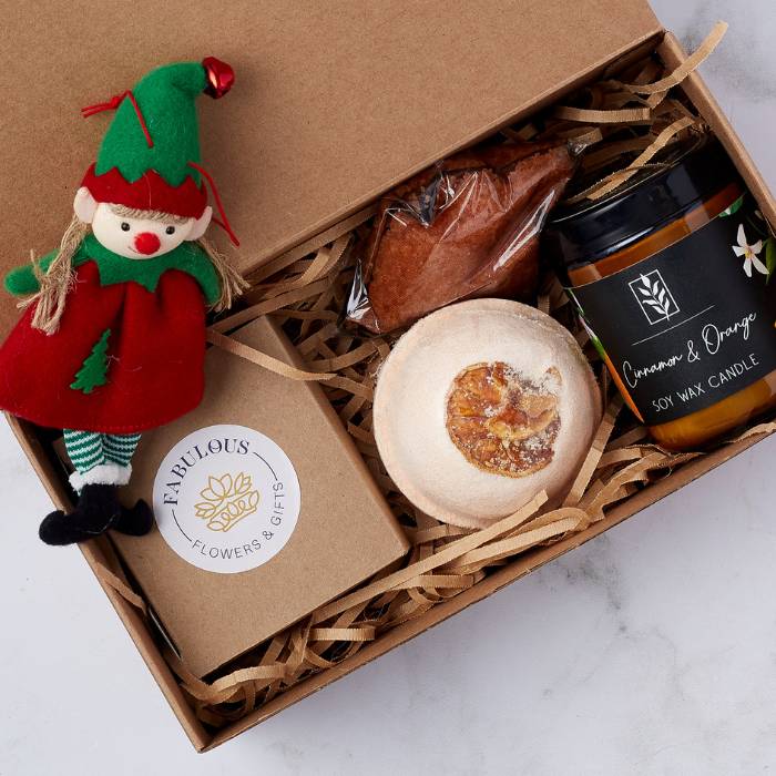 Festive Spice Glow Gift Set with cinnamon candle, orange bath bomb, hot chocolate mix, and elf ornament in a festive box.