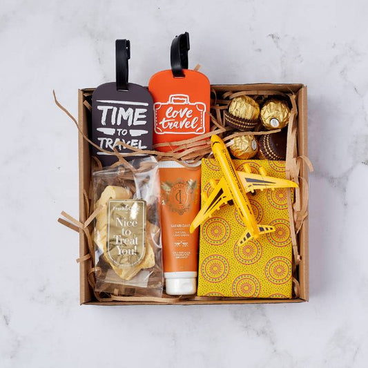 Travel-themed gift box featuring luggage tags, Safari Days hand cream, biscuit crisps, Ferrero Rocher chocolates, notebook, and toy plane.