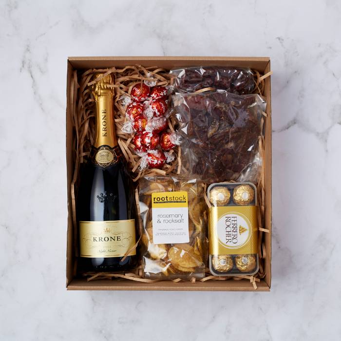 A luxurious snack hamper featuring a bottle of Krone Night Nectar MCC, Lindt Lindor truffles, Ferrero Rocher chocolates, handmade rosemary and rock salt potato crisps, and beef biltong, beautifully packaged with wood shavings.