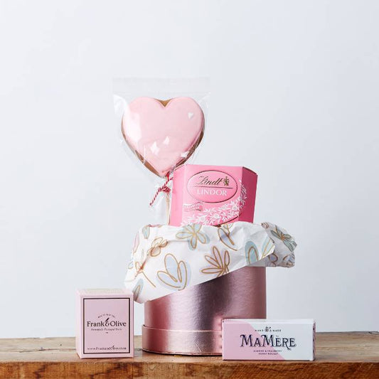 Close-up Love & Delight gift box by Flower Guy featuring a pink heart-shaped biscuit lollipop, Lindt truffles, Frank & Olive treats, and Ma Mère nougat.