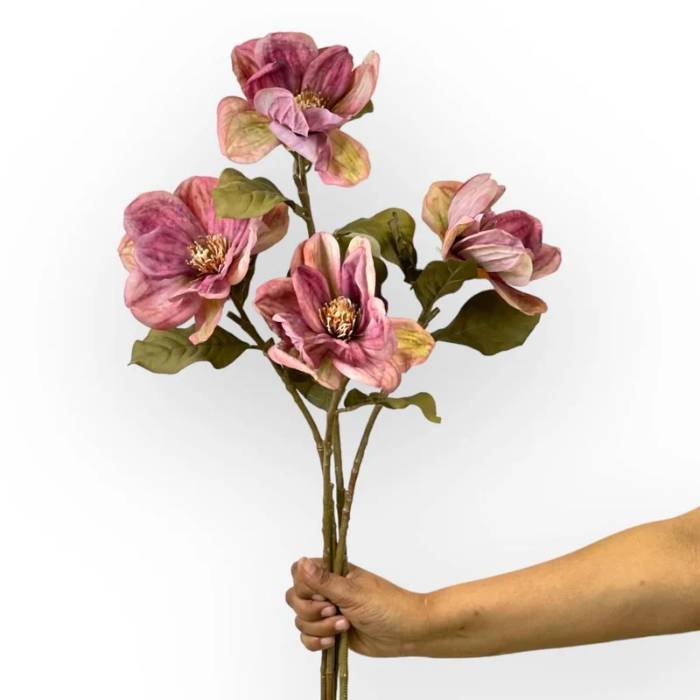 Hand holding a bouquet of Magnolia Dark Mauve Artificial Flowers with multiple mauve blooms and lush green leaves.