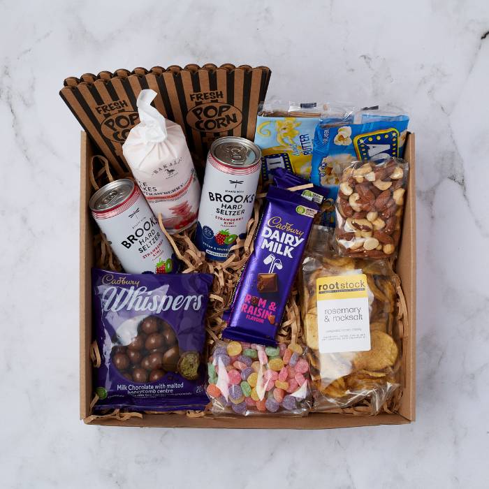 Movie Night Box featuring popcorn tubs, Brooks seltzers, chocolates, chips, and mixed nuts in elegant packaging.