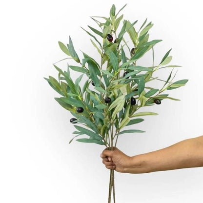 Hand holding a bouquet of Olive Branch Green Artificial Flowers featuring multiple stems with realistic green leaves and black olives.