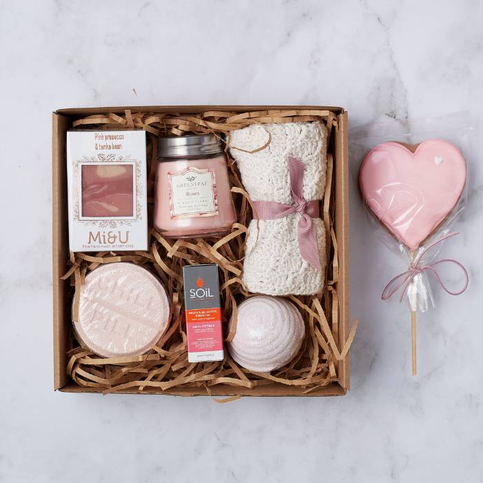 Pamper Perfection Gift Box filled with a knitted blanket, rose-scented candle, bath bomb, handmade soap, essential oil, and heart-shaped lollipop.