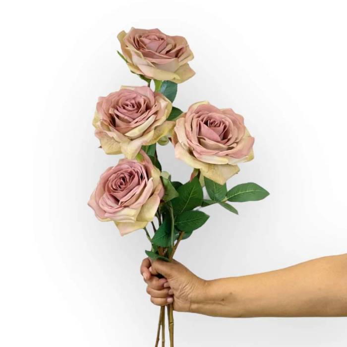 A hand holding a bouquet of four Rose Full Bloom Dusty Mauve Artificial Flowers with realistic leaves and stems.