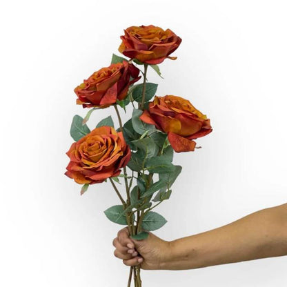 A bouquet of four Rose Full Bloom Rust Artificial Flowers held in one hand, showcasing rich rust-coloured petals and lush green leaves.