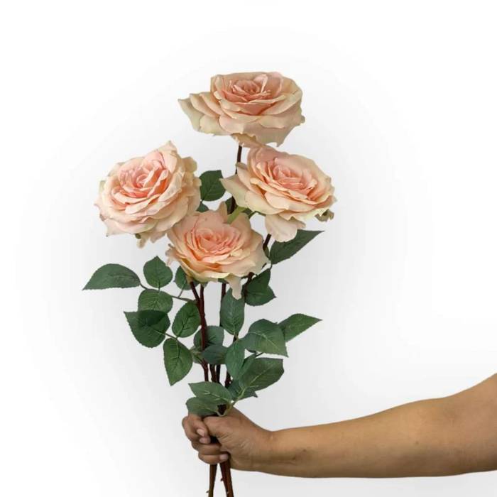 A hand holding a bouquet of four Rose Olivia Soft Pink Artificial Flowers, showcasing their delicate petals and soft pink hue.