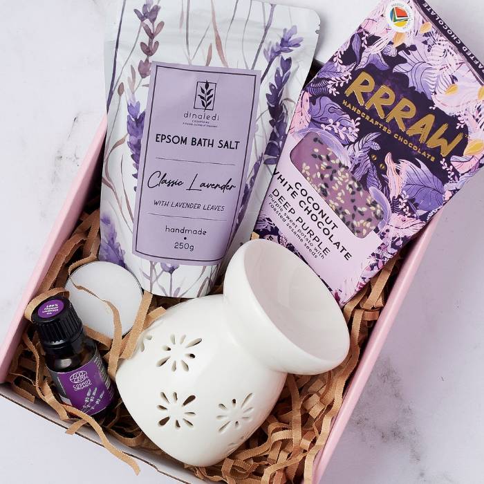 Close-up of Serenity Spa Gift Box with lavender bath salt, RRRAW coconut white chocolate, lavender oil, and ceramic oil burner.