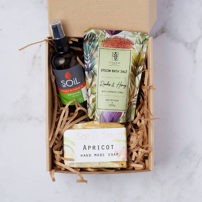 Serenity & Soothe Spa Gift Set featuring Soil massage oil, Dinaledi bath salt, and Salt & Stitch apricot handmade soap in a kraft box.