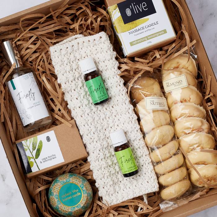 Close-up of Spa Day at Home Gift Box contents, including Firefly Ocean Room Spray, essential oils, massage candle, and almond biscuits.