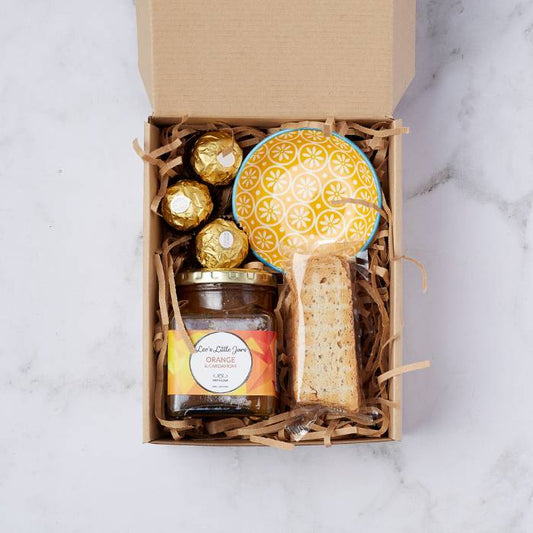 Gift box featuring orange and cardamom marmalade, Ferrero Rocher chocolates, crunchy biscotti, and a yellow hand-painted ceramic bowl.