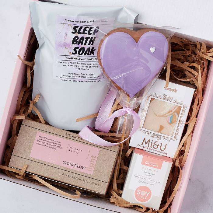 Close-up of Sweet Dreams Gift Box items, showcasing lavender bath soak, heart-shaped biscuit, Amandé artisan soap, soy candle, and floral-scented candles.