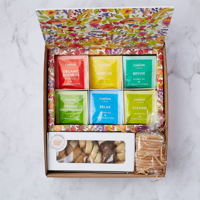 Top view of an open gift box containing a variety of Carmién Rooibos tea sachets and assorted biscuits.