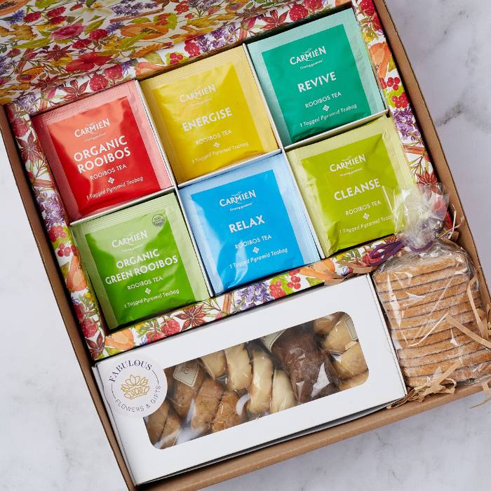 Close-up of Carmién Rooibos tea sachets and a selection of gourmet biscuits in a beautifully designed gift box.