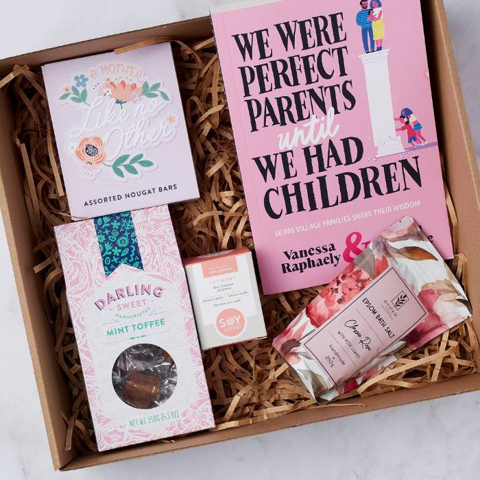 Close-up view of The Perfect Parent Pamper Gift Box items including a parenting book, sweets, candle, and bath soak.