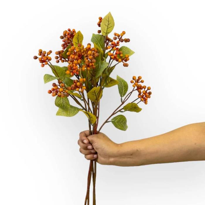 Hand holding a bouquet of Wild Berry Spray Rust Artificial Flowers by Flower Guy, featuring clusters of vibrant rust-coloured berries with green leaves.